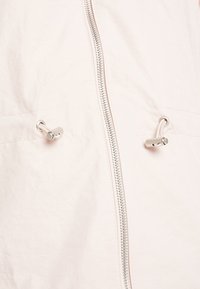 Ljusrosa jacka med dragkedja fram, justerbara dragsko och ett mjukt, något texturerat material. Minimalistisk design med silverfärgad detalj.