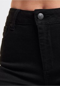 Svarte denimjeans med høy midje, med metallknapplukking preget med "DEF," og subtile sømdetaljer på lommene.