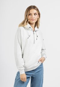 Felpa leggera grigia con zip frontale, cappuccio con cordino e polsini a coste. Abbinata a jeans in denim blu chiaro.