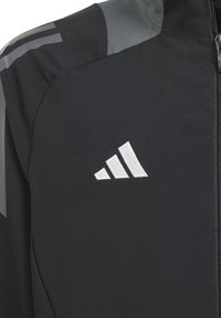 Veste de sport noire à la texture lisse, avec fermeture éclair et accents gris contrastants. Arborant un logo Adidas blanc sur la poitrine.