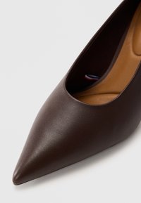 Brune skinnspiss pumps med en glatt tekstur; har en lav skjæring på sidene og en beige innvendig fôr.