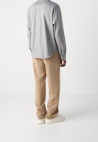Lichtgrijze lange mouwen shirt met een ronde zoom, beige broek en witte sneakers. Het materiaal lijkt zacht met een gladde textuur.