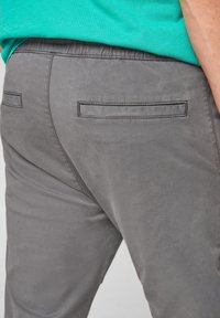 Grå bomullsblandade byxor med en slät textur, som har två bakfickor med rektangulära ficklock och en elastisk midja.