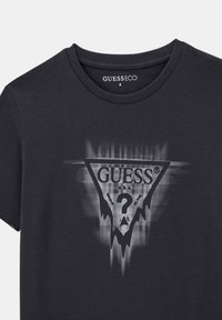 Černé bavlněné tričko s trojúhelníkovou grafikou a otazníkem a logem "GUESS". Krátké rukávy a kulatý výstřih.