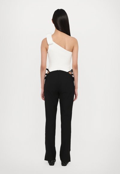Witte one-shoulder bodysuit gecombineerd met hoge zwarte broek met uitsneden aan de zijkanten en lintaccenten. Soepele texturen, aansluitend ontwerp.