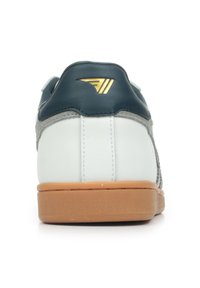 Sneaker bianco e grigio con tallone in pelle blu navy, dettagli del logo dorato e suola in gomma naturale. Sono visibili materiali lisci e testurizzati.