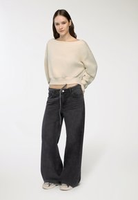 Felpa corta color crema con scollatura ampia, abbinata a jeans neri a gamba larga con cordoncino e tasche frontali, e sneaker color beige.