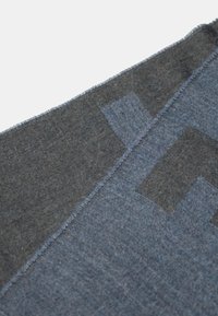 Sciarpa di tessuto blu con bordi sfrangiati, che presenta una combinazione di tonalità di blu più scure e più chiare, e motivi geometrici con texture diverse.