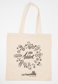 Borsa tote in tela beige con stampa grafica nera di vari sandali e il testo "100% Addict," insieme al logo del marchio in basso.