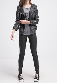 Černá kožená motorkářská bunda s prošívanými rameny, šedé tričko s grafickým potiskem a černé skinny kalhoty se zipovými detaily.