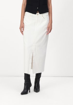 Vrouw die een witte midirok draagt met een voorste split, gecombineerd met zwarte hoge haklaarzen en een kort zwart vest.