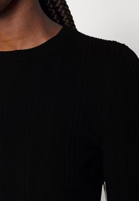 Czarny prążkowany top z długim rękawem, z okrągłym dekoltem i subtelną teksturą, podkreślający dopasowany krój i gładki materiał.