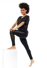Black athletic top with short sleeves and V-neck, paired with black leggings featuring a sheer panel on the sides, smooth texture throughout.