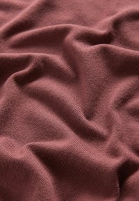 Pletivo v barvě zakouřené růže s měkkým, texturovaným povrchem, které má jemné záhyby a vrásky pro dynamický vizuální efekt.