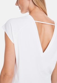 White short-sleeve top featuring a V-back design with a delicate strap detail and smooth texture, ideal for layering or casual wear.