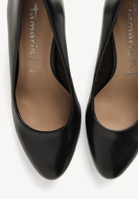 Black leather high-heeled shoes with pointed toes, smooth surface, and a natural inner lining. Features brand logo on the insole.