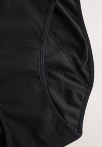 Suupilt mustast kangast, millel on õmmeldud õmblused ja riietel võrgust ventilatsioonipaneel, rõhutades tekstuuri ja konstruktsiooni detaile.