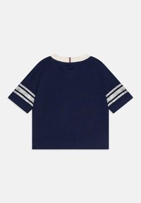 Marineblå t-skjorte med korte ermer, hvit crew neck og tre hvite striper på hver erme. Lett stoff med en jevn tekstur.