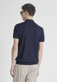 Polo shirt blu navy a maniche corte realizzato in un tessuto morbido e liscio, con colletto e orlo a coste. Indossato con pantaloni beige.