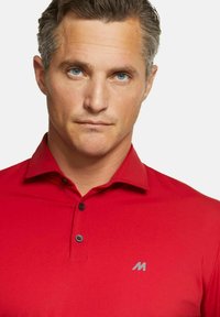 Rotes Poloshirt mit Kragen, zwei schwarzen Knöpfen und einem grauen Logo auf der linken Brust. Glatte Textur, taillierte Passform.