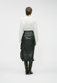 Green leather skirt with ruffled accents, high waist, and back zipper. Paired with a textured gray long-sleeve top and knee-high boots.