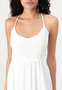 White dress featuring a knitted bodice and a crocheted waistband. The skirt is made from a lightweight, textured fabric with vertical pleats.