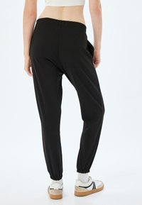Zwarte joggerpants met een elastische tailleband, taps toelopende boorden en zijzakken, gecombineerd met witte sneakers en witte sokken.