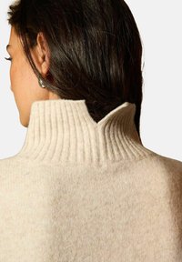 Sweter w kolorze kremowym z wysokim prążkowanym kołnierzem i dekoltem w kształcie łezki z tyłu. Miękka tekstura z delikatnie puszystym wykończeniem.