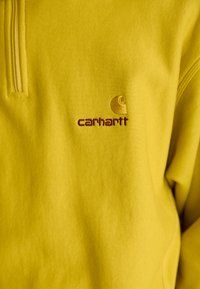 Gele sweatshirt met een halve rits; voorzien van een geborduurd logo in kastanjebruin. Soepele textuur met een losse pasvorm.