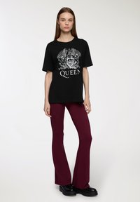 T-shirt grafico nero con design bianco "Queen", abbinato a pantaloni svasati borgogna e scarpe con platfform nere.