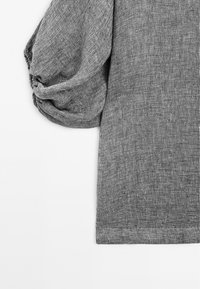 Top in tessuto grigio con una texture, caratterizzato da un design a maniche a sbuffo rilassate. Punti orlati e materiale morbido e traspirante con dettagli di pattern sottili.