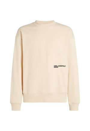 Bežs sporta krekls ar augstu apkakli, nolaistām plecu malām un ribotām aprocēm. Priekšpusē ir neliels melns "Karl Lagerfeld Jeans" logo.
