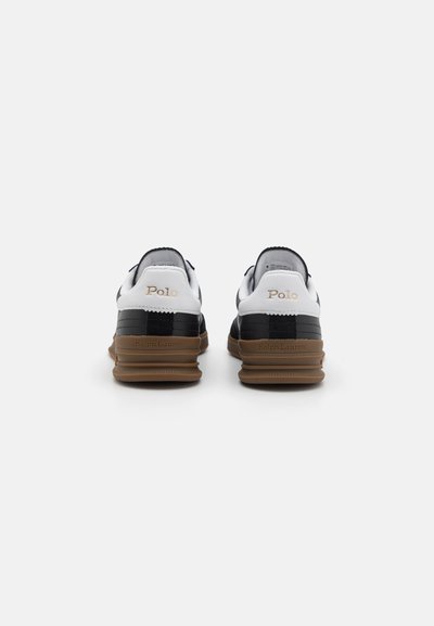 Witte en zwarte leren sneakers met een bruine rubberen zool. Kenmerken zijn logo-accenten aan de achterkant en textuurdetails op de bovenkant.