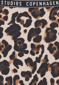 Tkanina z leopardjim vzorom, ki ima bež ozadje z temno rjavimi in črnimi pikami. Mehka struktura z elastičnim pasom, na katerem je napis "STUDIOS COPENHAGEN."