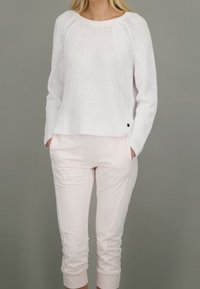 Weißer gestrickter Pullover mit lässiger Passform und gerippter Textur, kombiniert mit hellrosa, schmal zulaufenden Sweatpants mit seitlichen Taschen.