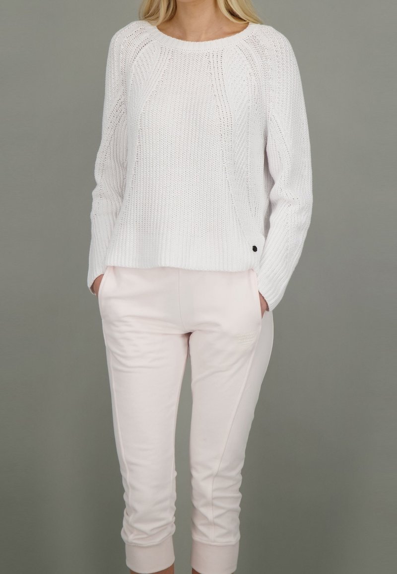 Weißer gestrickter Pullover mit lässiger Passform und gerippter Textur, kombiniert mit hellrosa, schmal zulaufenden Sweatpants mit seitlichen Taschen.