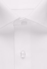 Camicia bianca con colletto caratterizzata da una texture liscia a tessuto semplice, con bottone in plastica trasparente e dettaglio di cuciture rinforzate.