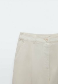 Hoge taille crèmekleurige broek met knoopsluiting en riemlussen, voorzien van zijzakken en geplooid detail aan de voorkant.