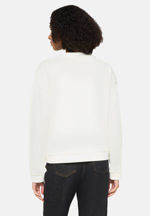 Licht crèmekleurige sweatshirt met een ontspannen pasvorm, geribde boorden en zoom, verzonken schoudernaden en een zachte textuur, gecombineerd met donkere spijkerbroek.