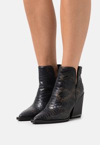Botas negras de tobillo con un patrón de piel de serpiente, punta afilada, tacón de cuña de altura media y detalle lateral recortado para mayor estilo. Material de cuero texturizado.