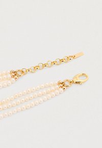 Κολιέ με στρώσεις από μαργαριτάρια, που διαθέτει πολλαπλές σειρές εκρού μαργαριταριών, με εξαρτήματα σε χρυσό τόνο και κούμπωμα με κλιπ αστακού.