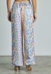 Pantalons larges à motifs géométriques colorés avec une taille élastique, fabriqués dans un tissu lisse et léger aux teintes de violet, orange et bleu-vert.