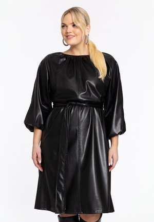 Robe noire en simili cuir avec une taille cintrée, des manches bouffantes et un col rond ; présente des coutures verticales et une texture lisse.
