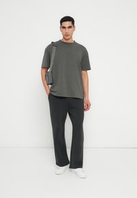 Szary, oversize'owy T-shirt z okrągłym dekoltem, w połączeniu z ciemnoszarymi dresami i białymi trampkami. Modelka nosi małą torebkę na ramię.