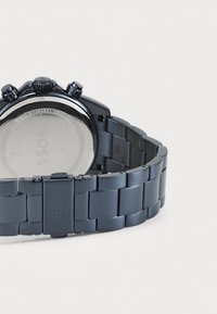 Μαύρο ρολόι από ανοξείδωτο ατσάλι με απαλό, ματ φινίρισμα, διαθέτει υφασμένη βραχιολάκι, τρία κουμπιά χειρισμού και γυαλιστερό πίσω μέρος της κάσας.