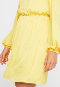 Vestido amarillo con mangas largas y abullonadas y una cintura elástica. Hecho de una tela ligera, con una textura suave y un diseño fluido.
