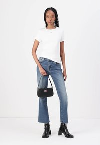 Maglietta bianca a maniche corte, jeans blu a gamba dritta, stivaletti neri alla caviglia e una borsa nera con dettaglio del logo colorato.