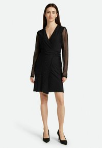 Schwarzes Cocktailkleid mit Wickeldesign, langen transparenten Ärmeln und verstreuten Strassverzierungen. Glatte Textur, knielanger Saum.