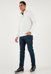 Biely rebrovaný pulóver s golierom na štvrtinový zips, doplnený tmavomodrými slim-fit džínsami a teniskami s šedými akcentmi. Hladká textúra a ležérny dizajn.