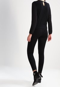 Maglia nera a maniche lunghe con schiena a chiave, abbinata a jeans neri aderenti e stivaletti con dettagli decorativi. Tessuto liscio e vestibilità sagomata.